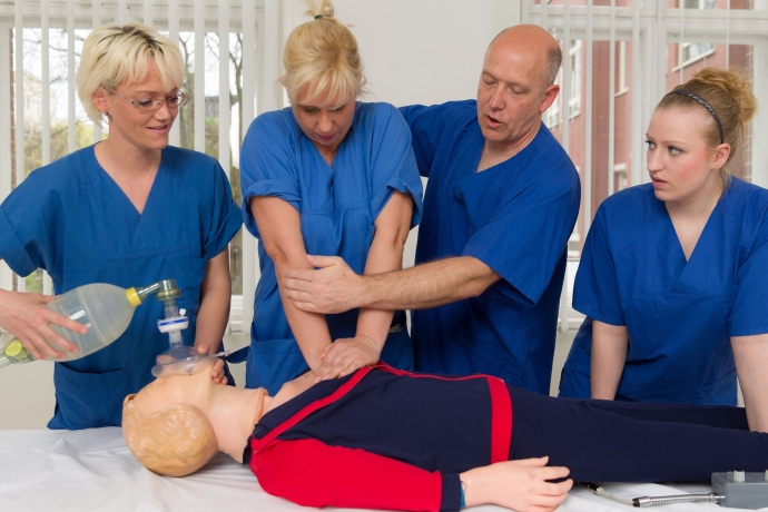 Vier Pflegekräfte üben Herzdruckmassage an einer Puppe